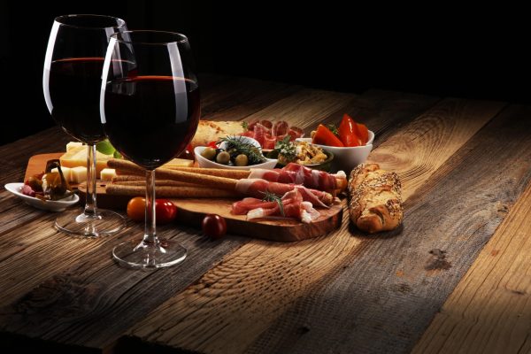 Italian antipasti wine snacks set. Cheese variety, Mediterranean olives, crudo, Prosciutto di Parma, salami and wine in glasses over wooden grunge background
